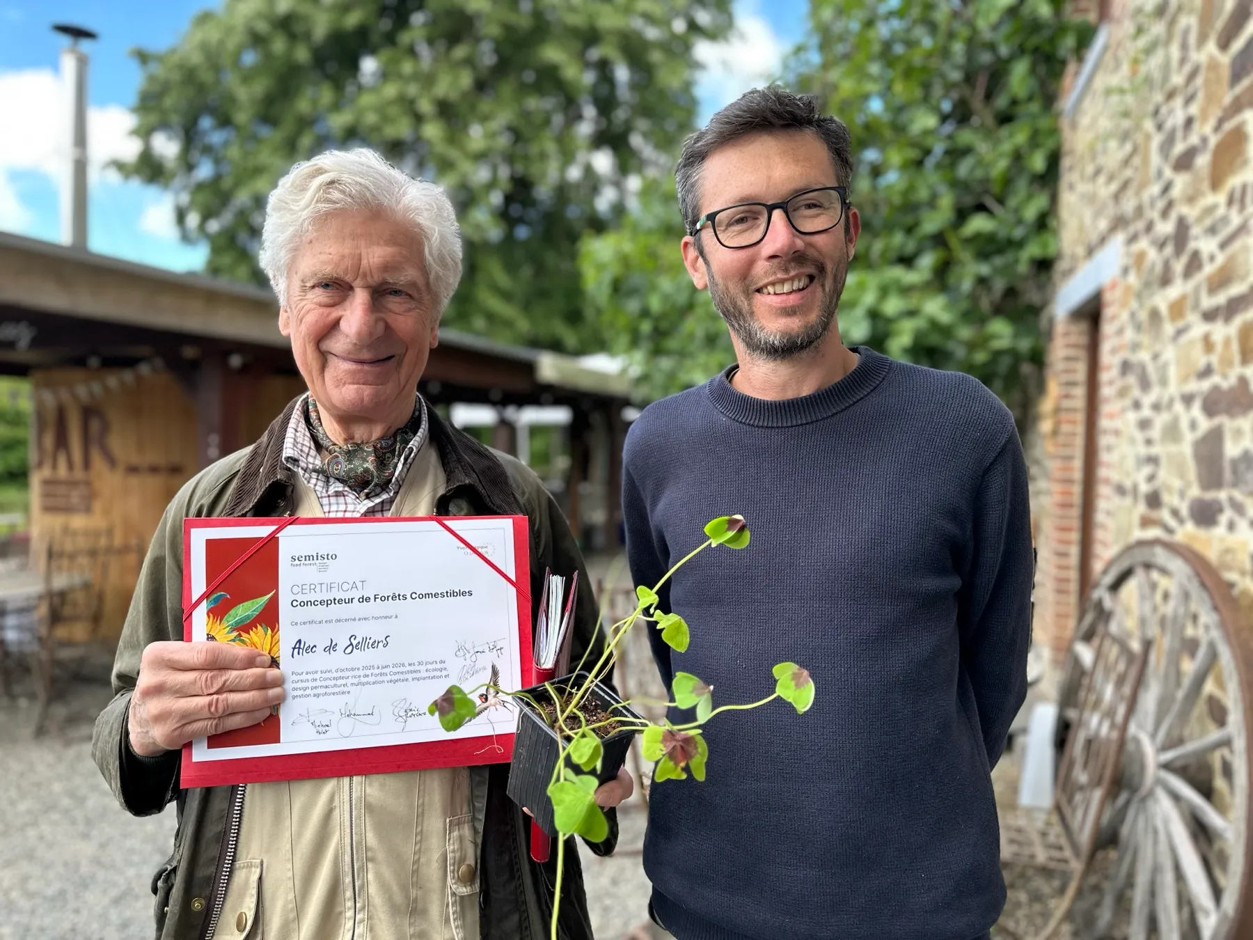 Alec de Selliers smiling, holding his Food Forest Designer certificate, next to Michael Hulet, Semisto's founder