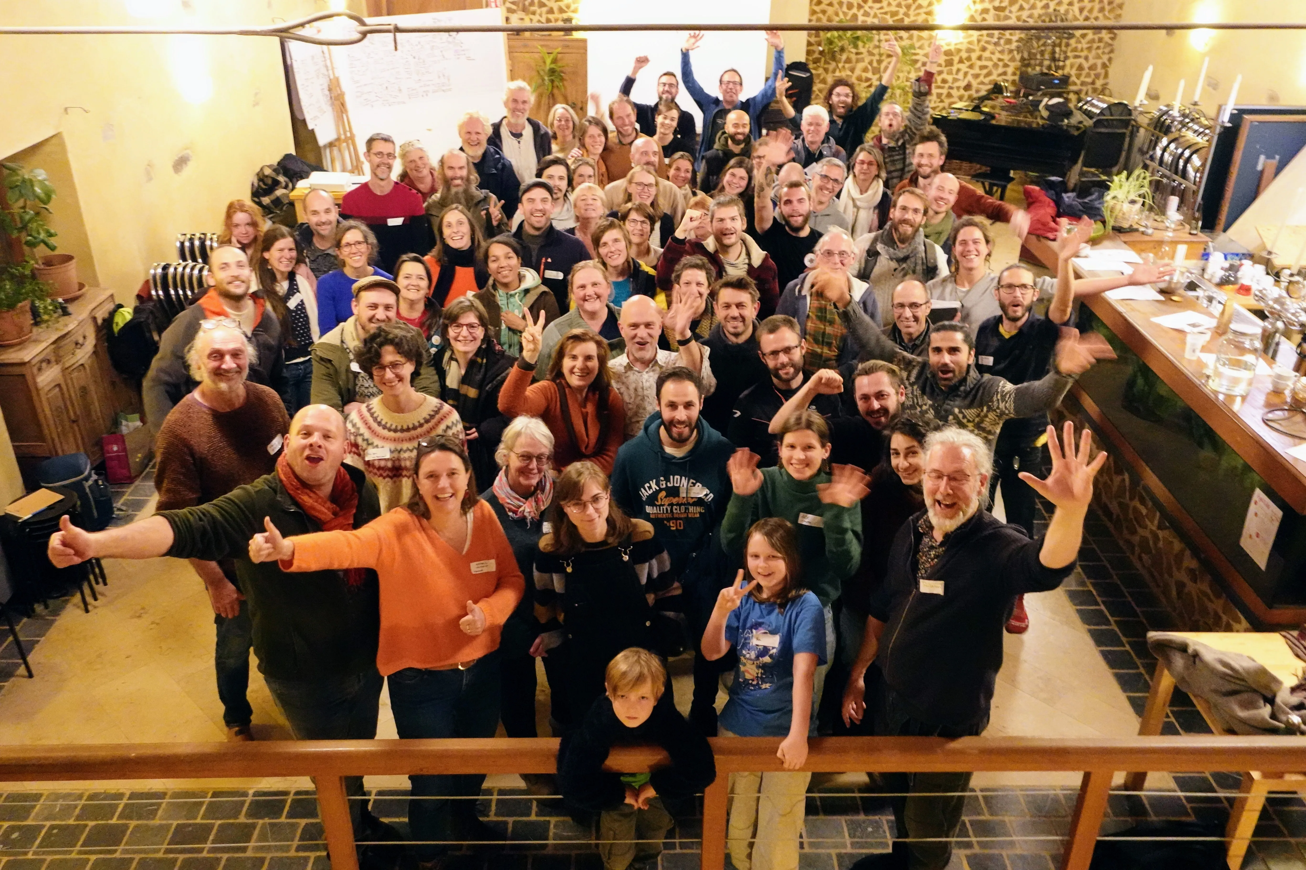 Large joyful group gathered in a warm room, arms raised