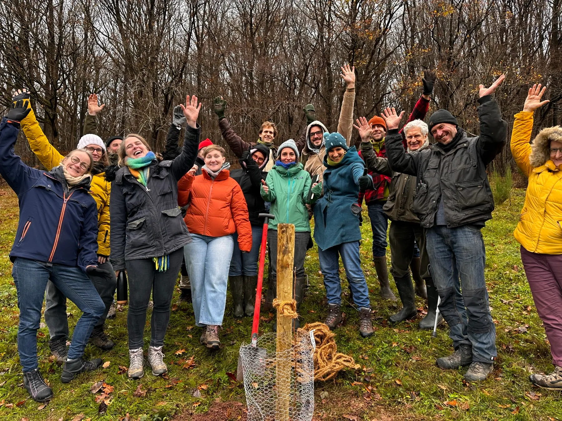 The program's cohort, Alec among them, arms raised around a young tree freshly planted on a winter's day