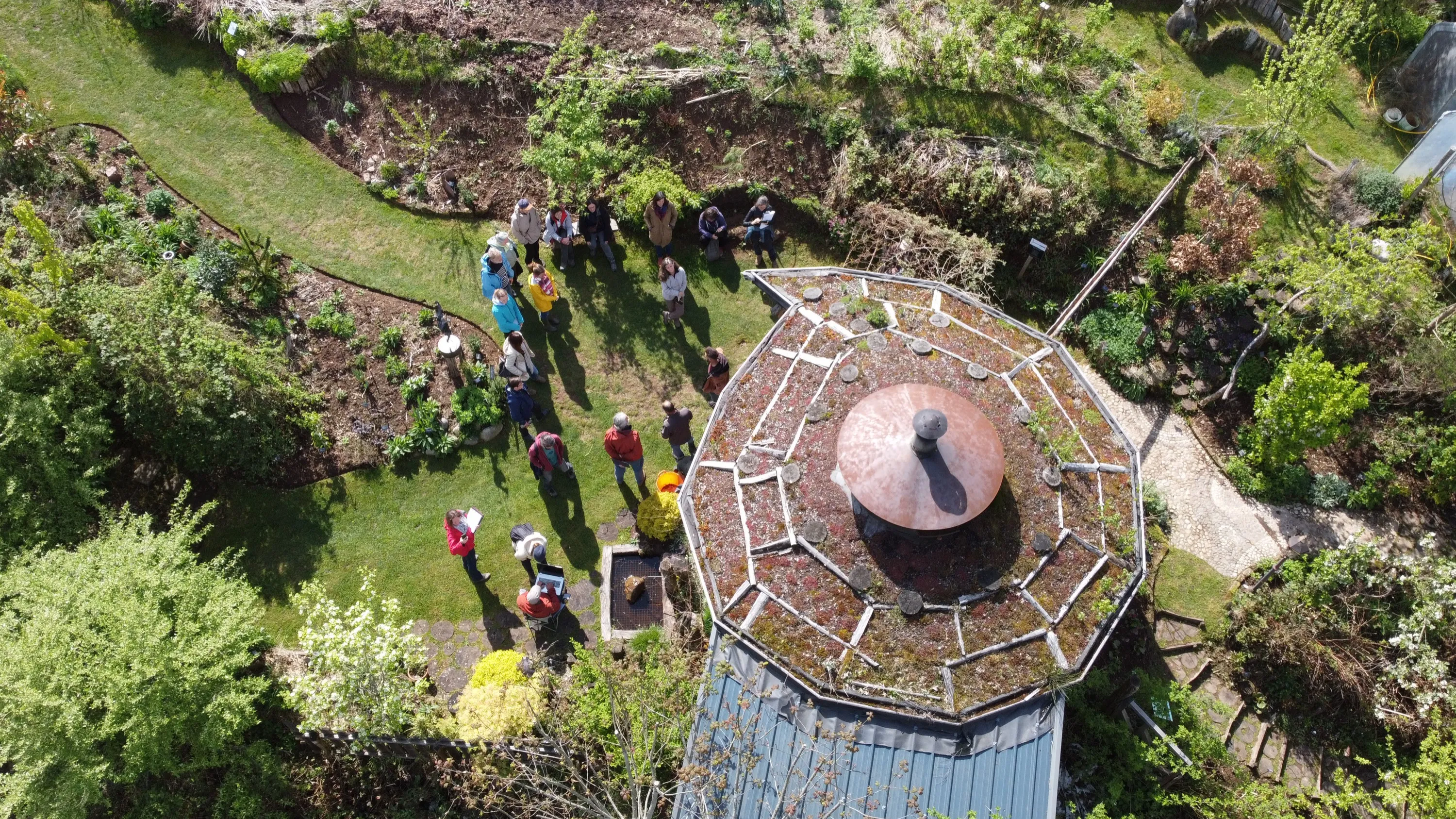 Vue aérienne d'un jardin-forêt mature : le groupe en visite près d'un kiosque au toit végétalisé