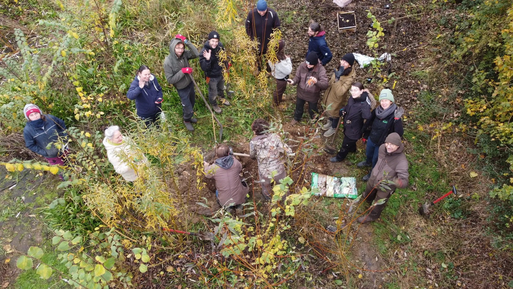 Vue aérienne d'un chantier participatif : une quinzaine de bénévoles plantent ensemble dans le jardin-forêt