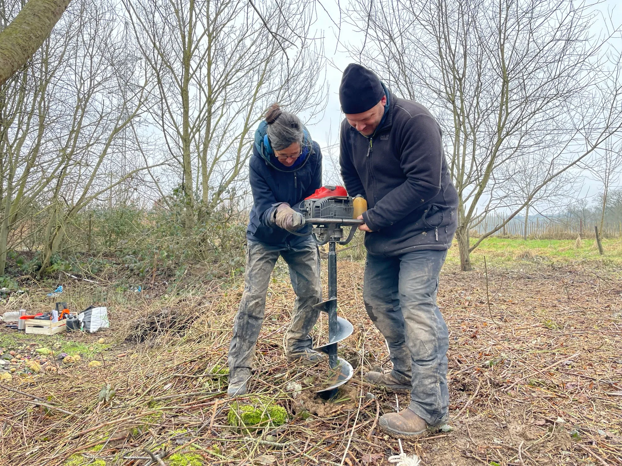 Deux membres de l'équipe percent le sol à la tarière thermique pour planter un arbre